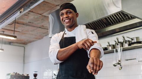 chef wearing a chef coat and apron standing in front of a rack of pots and ladles